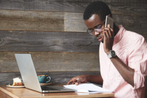 Young African executive officer in formal shirt examining a financial report, making phone calls to